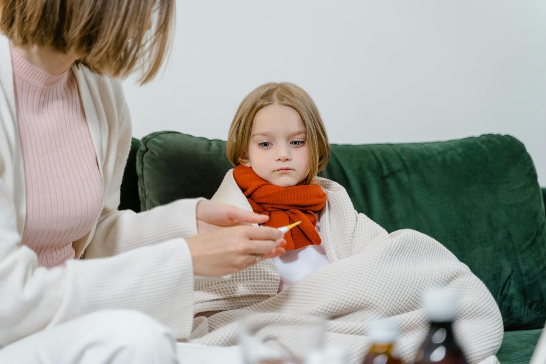 doctor checking the temperature of her child patient while sitting on green couch doctor checking the temperature of her child patient while sitting on green couch doctor checking the temperature of her child patient while sitting on green couch
